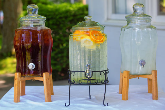 Three glass juice containers containing three different drinks. The first container contains a dark red juice, the second a clear liquid with slices of orange. The third container has a cloudy clear liquid. 